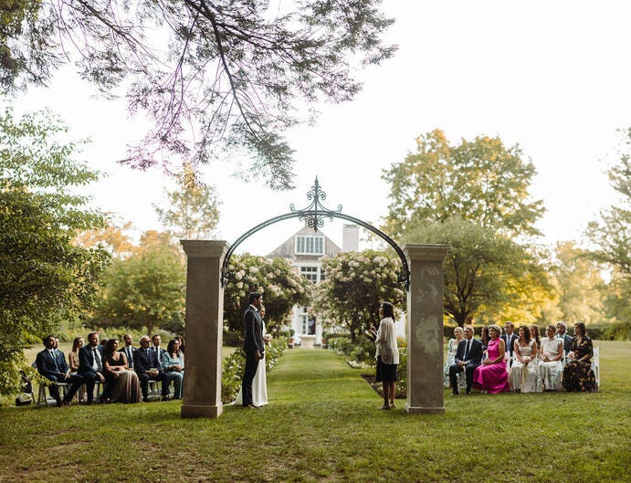 Bride and groom stand before their guests at an outdoors, masked and socially distant 2020 Covid Wedding.