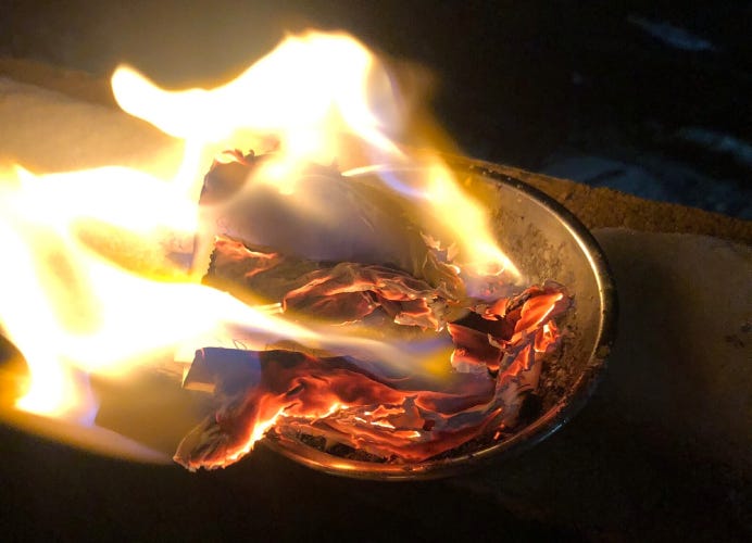 A stainless steel bowl holding a piece of notebook paper in flames