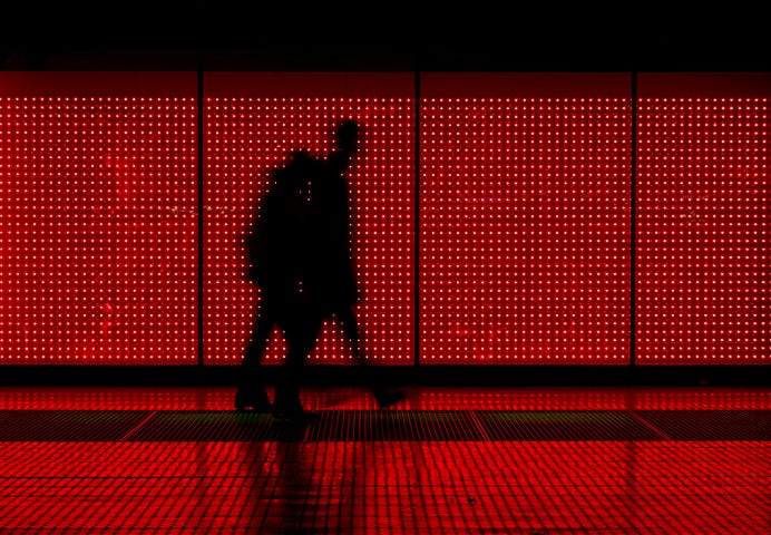 Two people walking, silhouetted against a wall covered with small red lights.