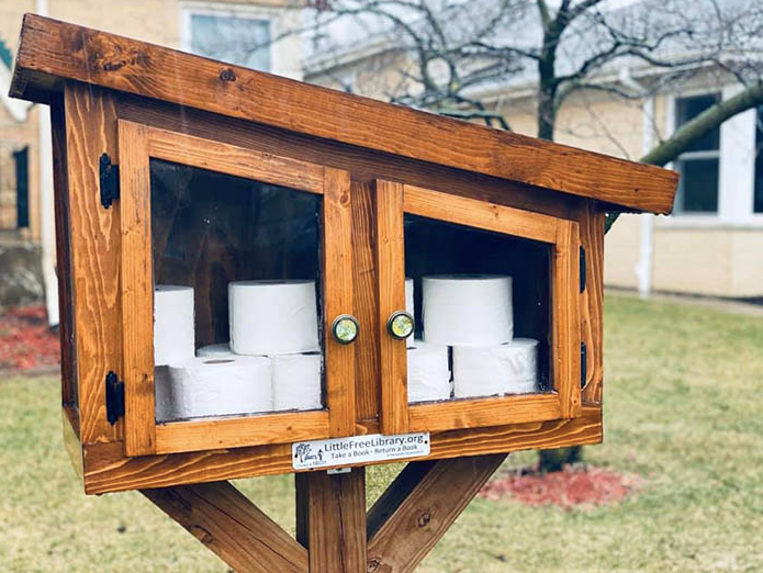 A Little Free Library box containing toilet paper and other goods.