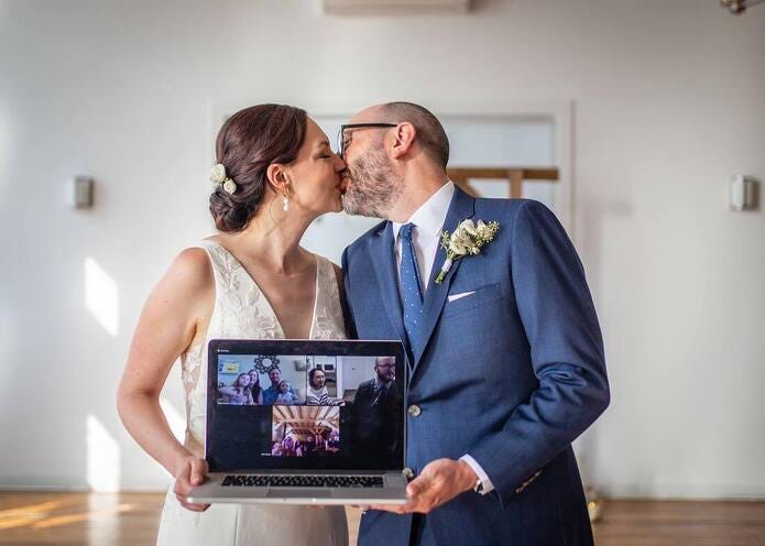 Bride and groom kiss while holding a laptop showing their Zoom wedding guests at a 2020 Covid Wedding.