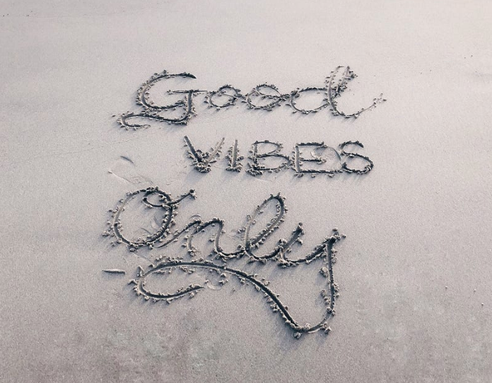 The words Good Vibes Only are drawn into sand.