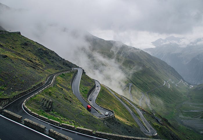 photograph of cars winding up a mountain road with a series of hairpin turns and switchbacks.