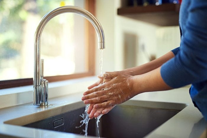 Shot of an unrecognizable woman washing her hands in the kitchen sink