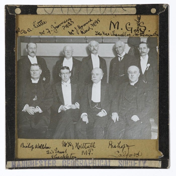 A photographic slide of select members of the Manchester Geographical Society in Victorian formal dress. They include the Vice Chancellor of the University, a local M.P. and the Bishop of Salford. They are accompanied by explorer Ernest Shackleton.