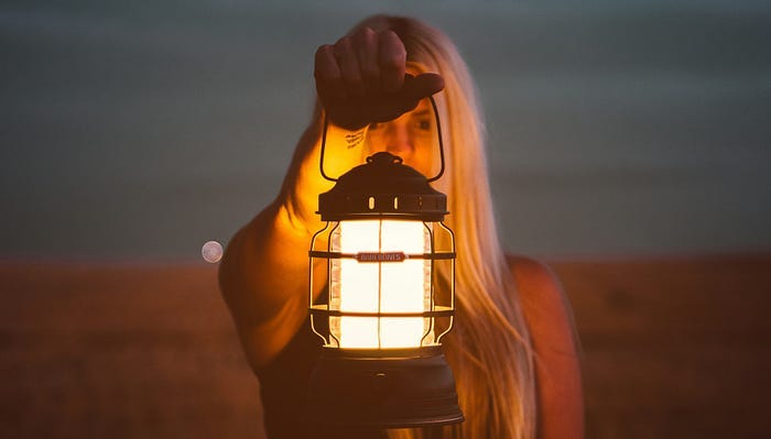 Woman holding a lantern outside at night. She tries to look into the future to see how things turn out.