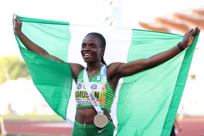 A black woman holding the Nigerian flag with a medal over her neck