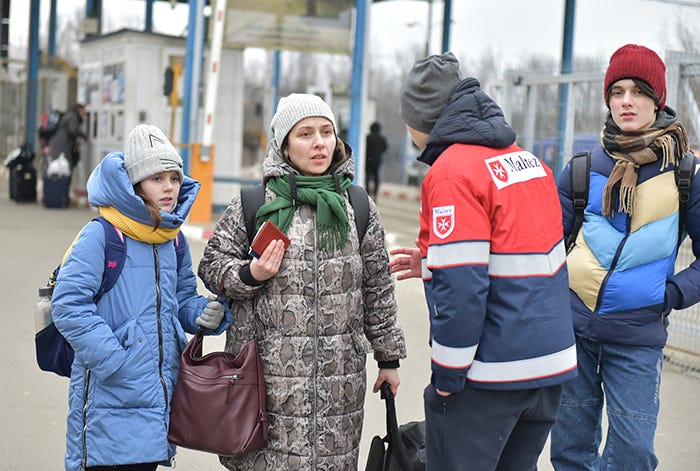 From left to right: A Ukrainian girl wearing a blue jacket and yellow scarf, a Ukrainian woman wearing a brown jacket, a volunteer wearing a red and blue jacket, and a Ukrainian boy wearing a blue-and-yellow jacket, in the border town of Siret, Romania.