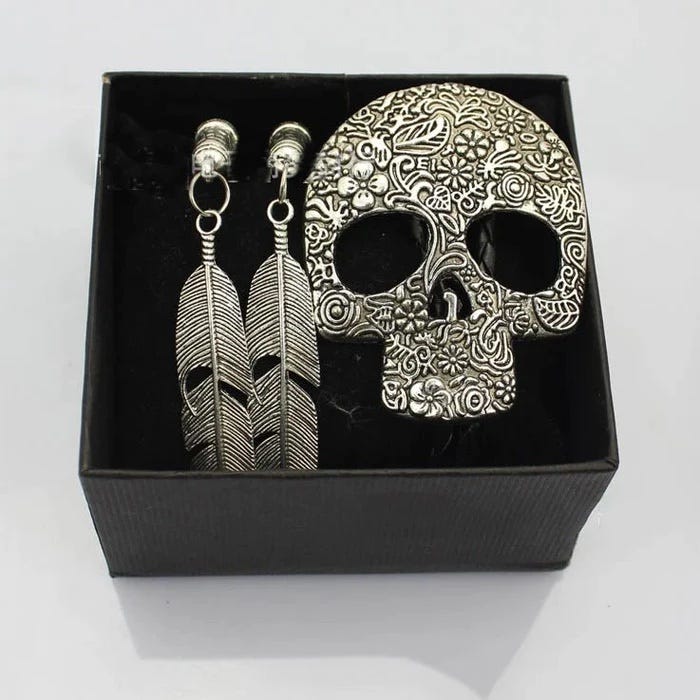 A silver Calavera Sugar Skull designed unisex bolo tie with feather tips in a black gift box.