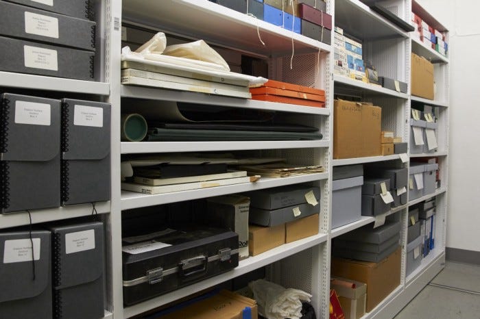 View of special collections material, boxes of all sizes on white shelving.