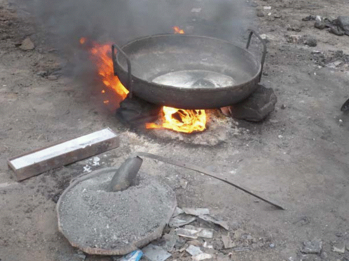 A large pan with liquid metal in it on top of a fire on the ground