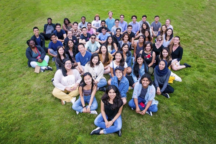 A group of around 30 young adults sit on grass.