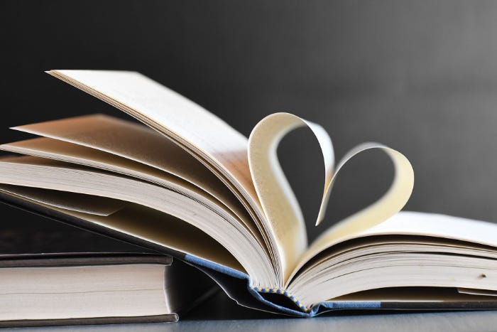 Two books, one open and leaning on the first book, with two pages folded into the shape of a heart.