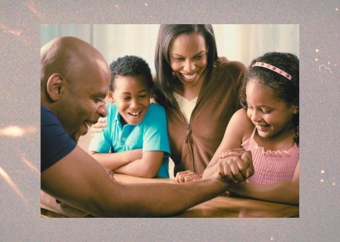 a father and daughter arm wrestling while the mother and brother cheer them on