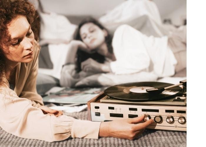 a stylized photo with women lounging, blurred out, in the background and a woman in the foreground adjusting a record player