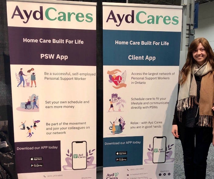 Multitalented UI/UX Designer Maria Vassilieva standing proud beside two banners she designed for Ayd Cares.