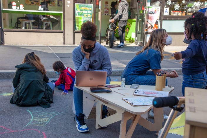 Many people sitting around talking or using computers outside.