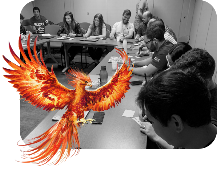 Imagem em preto e branco de uma sala com mais de 20 pessoas participando de uma dinâmica. Em primeiro plano há uma ave Fênix.