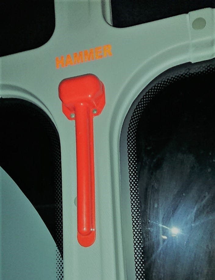 A hammer on the bus to break glass during an emergency. The hammer is screwed to the side, with a plastic lid covering it.