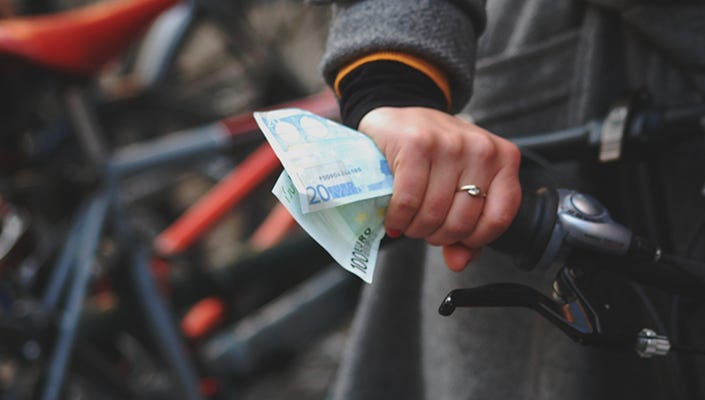 A woman’s hand on a bicycle handlebar while holding cash at the same time