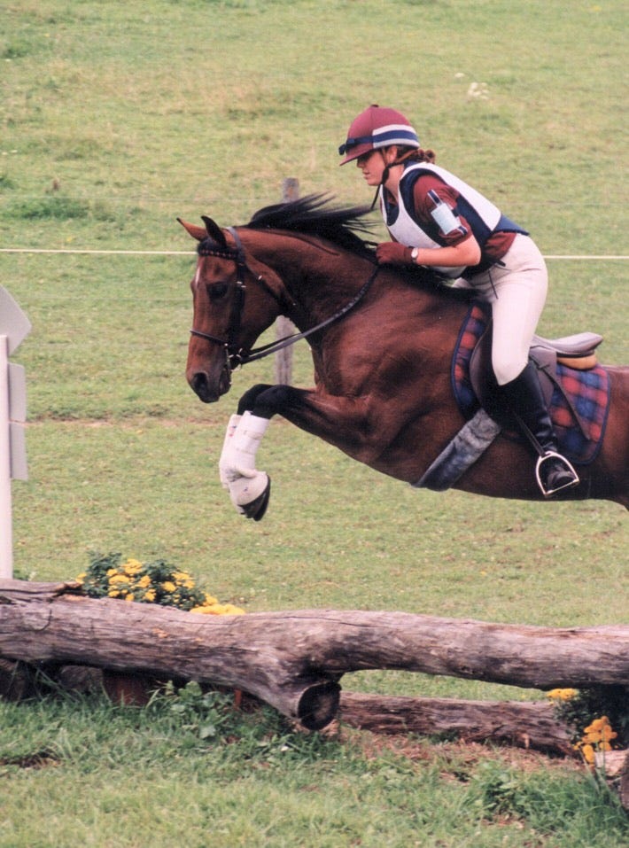 A woman is riding a horse as they jump over an obstacle.