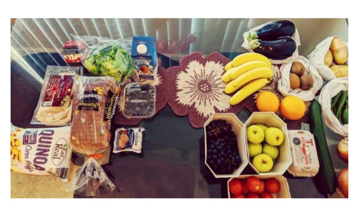 Groceries displayed on a table. Fruit and vegetables on one side with produce packaged in plastic on the other.