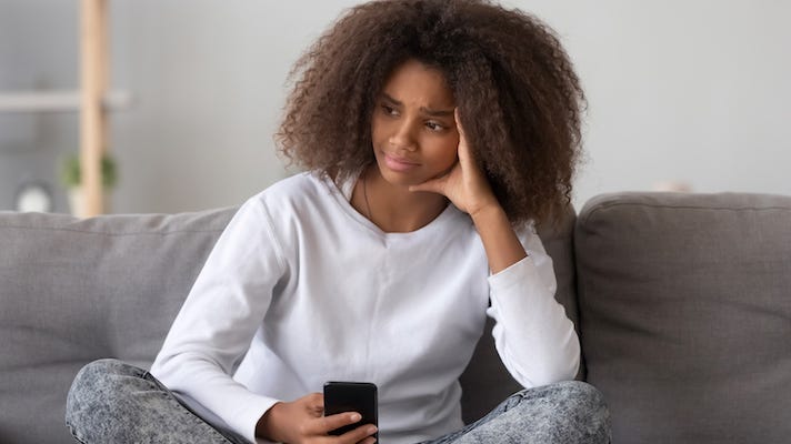 young sad, anxious girl on couch with phone in hand