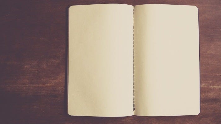An open, unlined, blank journal on a wooden desktop.