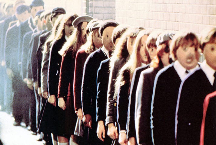 Cena do filme “The Wall”. Estudantes estão enfileirados, usando máscaras e roupas iguais. Não há diferenciação.