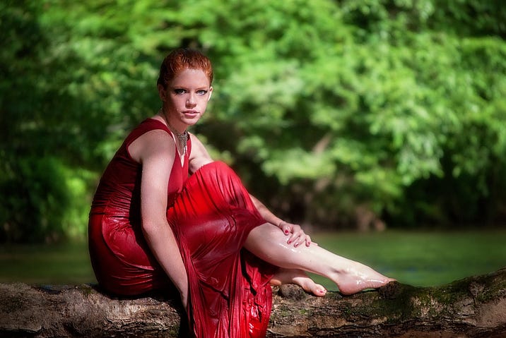 Woman in red dress sitting my a river with bare feet