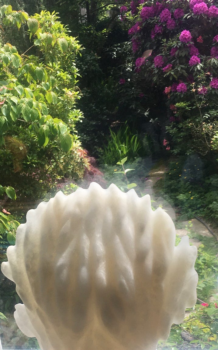 Two joined hands engulfed in flames carved from alabaster. The garden has various shapes of foliage, flowers and a path