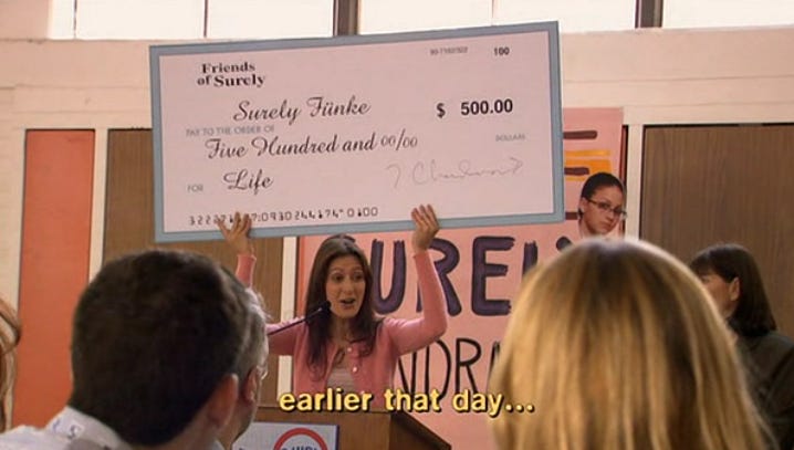 A representative from Friends of Surely holds up a giant check for five hundred dollars for Surely Fünke for life.