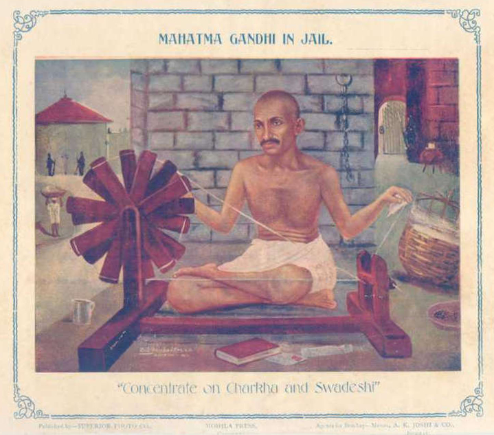 A vintage illustration of Mahatma Gandhi in jail, seated cross-legged and spinning yarn on a charkha. The background shows prison walls and guards. The caption reads, ‘Concentrate on Charkha and Swadeshi,’ emphasizing self-reliance and the Swadeshi movement.