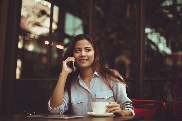 Photograph of a woman drinking coffee outside and speaking on her cell phone