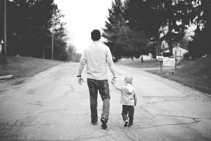 A father and child holding hands while walking down a road.