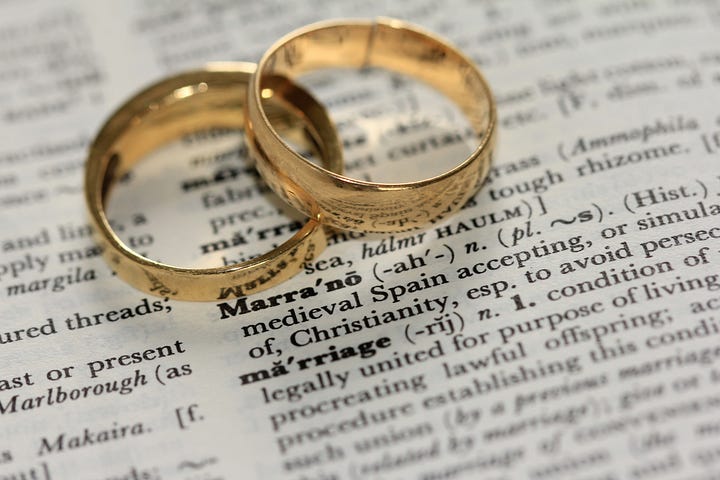 Two gold wedding bands lying on a dictionary page open to the definition of marriage.