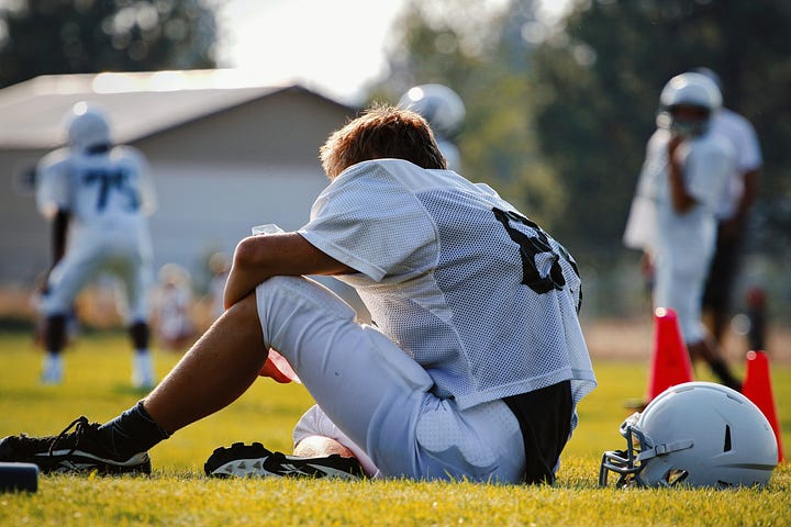Young football player sitting on the grass while others play