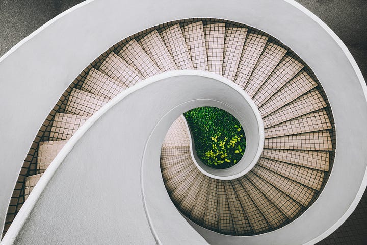 a curving beige stairway with a center filled with green plants.