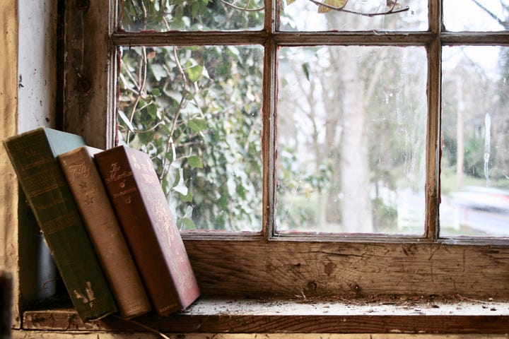 An old pile of books standing on a windowsill.