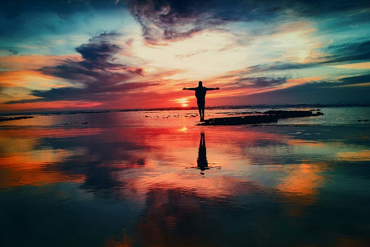 A silhouette of a person praising God during sunrise at the beach with a beautiful colorful sky.