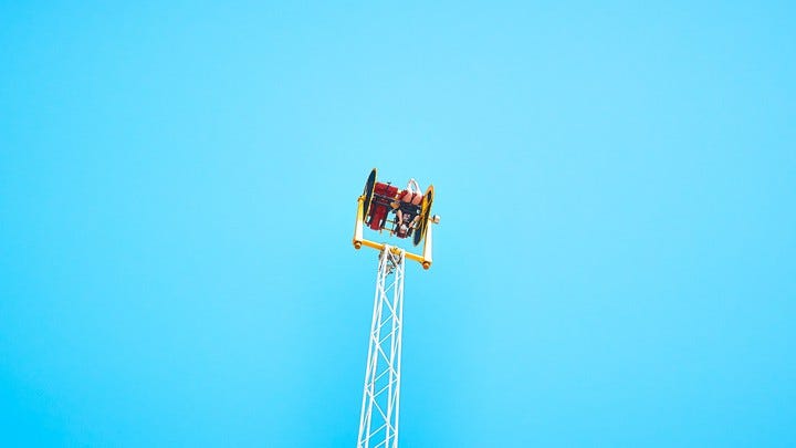 A person on a two-seater carnival ride that flings people upside down, which it is currently doing in front of a cloudless blue sky.