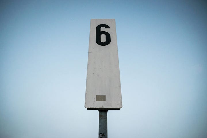 A sign on a pole with the number six written on it.