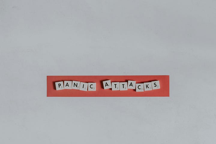 Photo of a white wall with the phrase in letters of scrabble style “Panic attacks” in a red stripe.