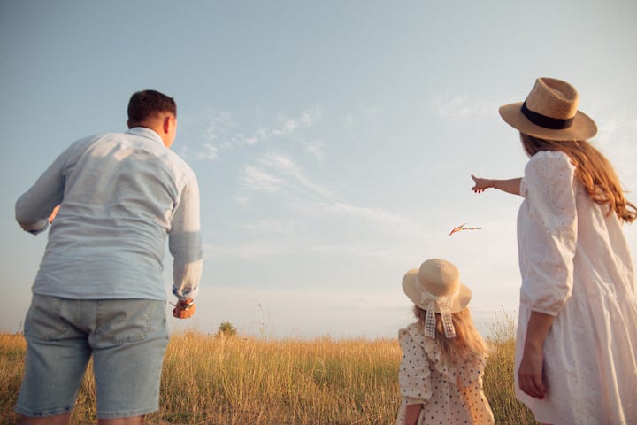 A man and woman with a small girl out in a field fly a kite.