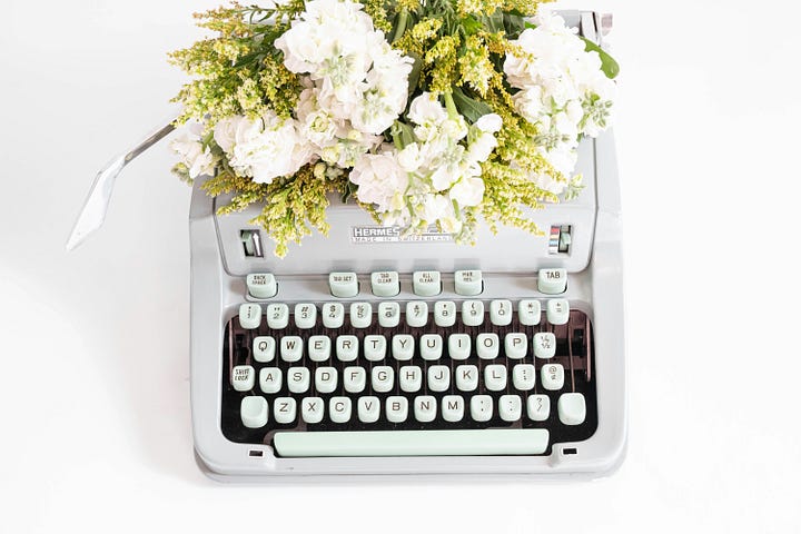 A white metal typewriter has been decorated with a bouquet of fresh white flowers.