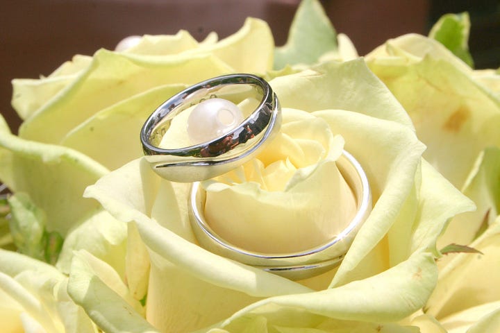 Photo of a cluster of yellow roses with his and her wedding bands in the center.