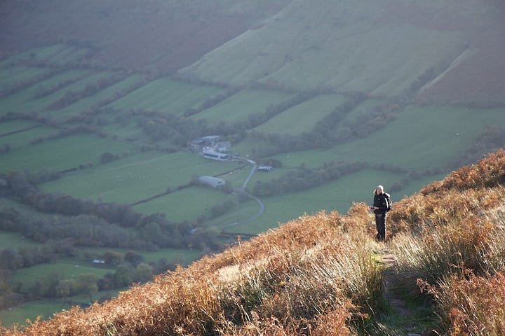 Picture of a walker on a hill side with a farm in a valley far below and behind