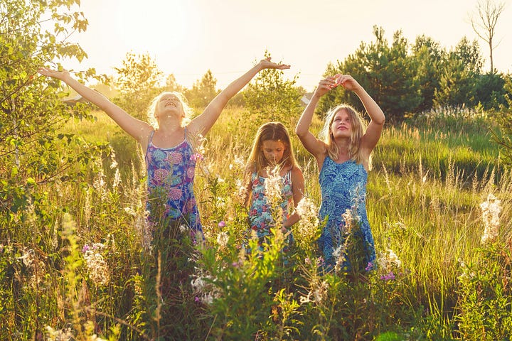 Three girls in sundresses, playing in a sun-drenched field of flowers.