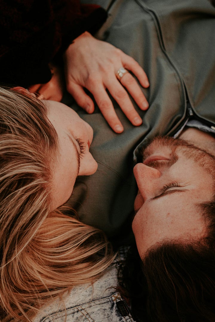 Married couple lying in each other&rsquo;s arms with gentle smiles on their faces.