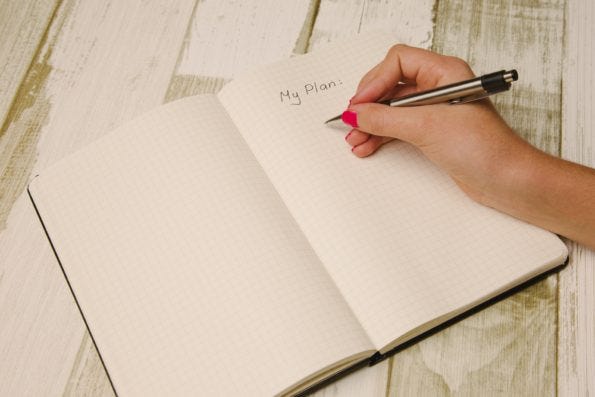 A diary open with the words 'my plan' on in handwriting with a hand holding a pen hovering over it